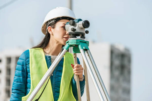 Surveyor em hardhat e jaqueta de alta visibilidade olhando em nível digital — Fotografia de Stock