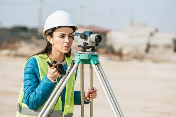 Agrimensora femenina con equipo de radio mirando a través del nivel digital - foto de stock