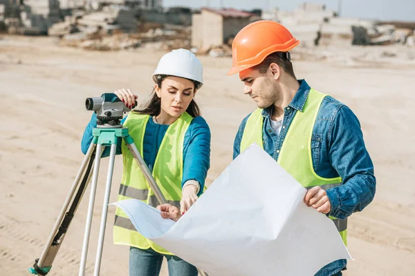 Surveyor avec le niveau numérique pointant sur le plan à collègue — Photo de stock