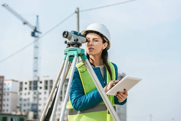 Surveyor with digital tablet looking through measuring level on construction site — Stock Photo
