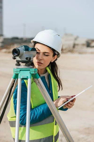 Vermessungsingenieur mit digitalem Tablet schaut durch Messpegel — Stockfoto