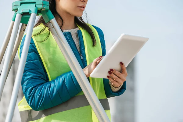 Cropped view of surveyor using digital tablet beside measuring level — Stock Photo