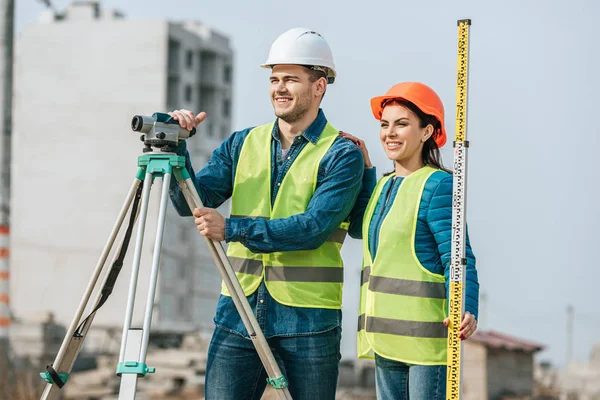 Smiling surveyors with ruler and digital level looking away — Stock Photo