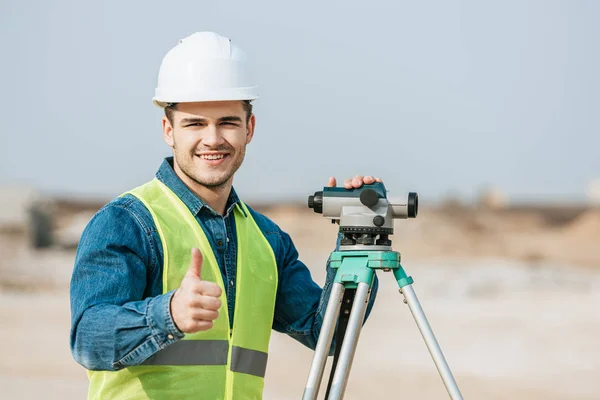 Smiling surveyor with digital level showing thumb up gesture — Stock Photo