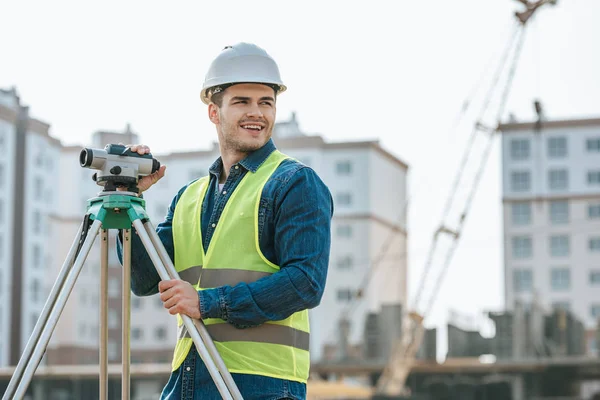 Surveyeur souriant avec niveau numérique regardant loin sur le chantier de construction — Photo de stock
