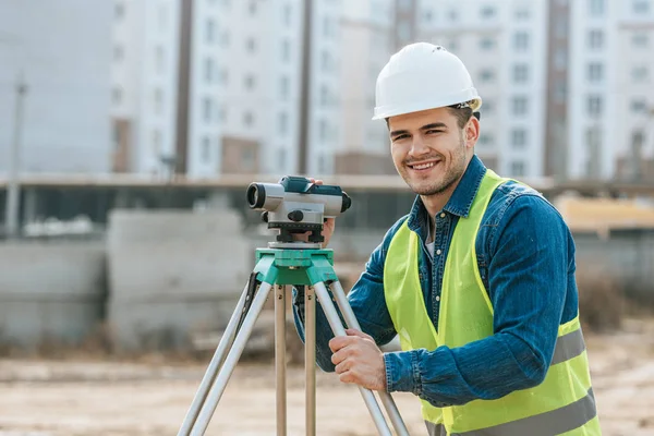 Inspetor sorridente com nível digital olhando para a câmera no canteiro de obras — Fotografia de Stock