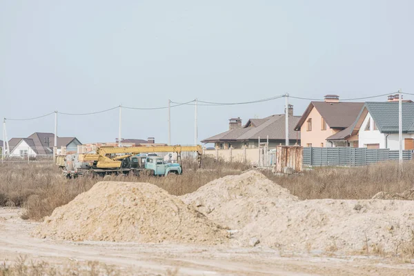 Moldes de areia na estrada de terra com guindaste de construção e casas no fundo — Fotografia de Stock