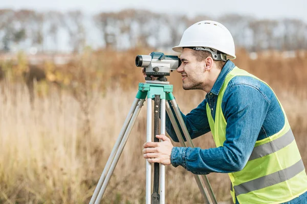 Side view of surveyor looking through digital level in field — Stock Photo