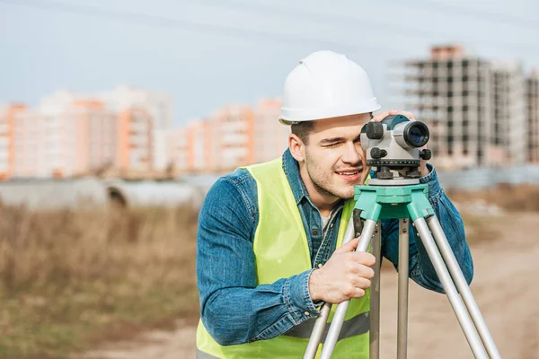 Lächelnder Vermessungsingenieur in Bollenhut und Warnweste, der durch die digitale Ebene schaut — Stockfoto