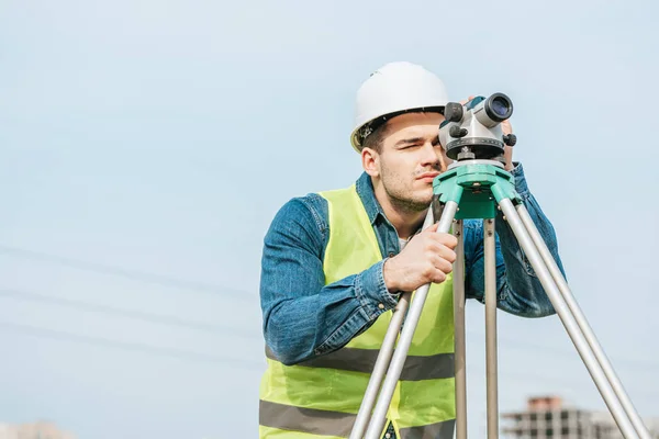 Surveyor en hardhat y chaqueta de alta visibilidad mirando a través del nivel digital - foto de stock