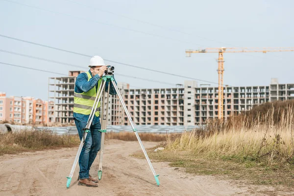 Vermessungsingenieur schaut sich digitalen Pegel auf Feldweg der Baustelle an — Stockfoto