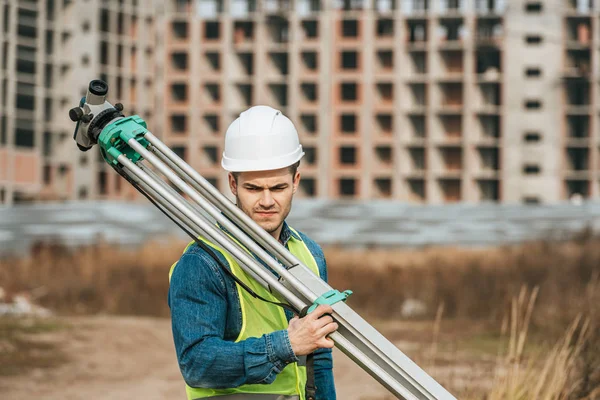 Pensive surveyor holding digital level with construction site at background — Stock Photo