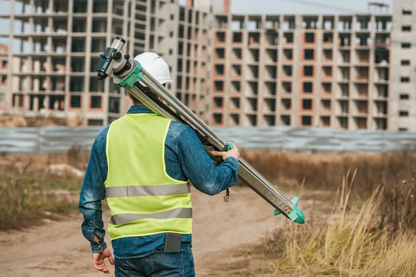 Rear view of surveyor holding digital level with construction site at background — Stock Photo