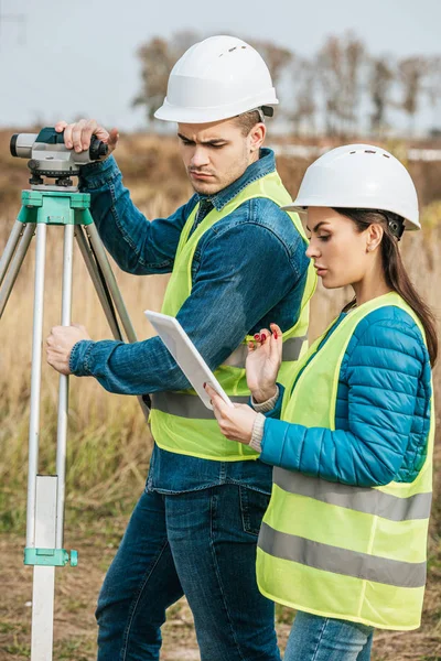 Inquéritos com nível digital olhando para tablet em campo — Fotografia de Stock