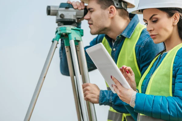 Enfoque selectivo en topógrafo con tablet y colega con nivel digital - foto de stock