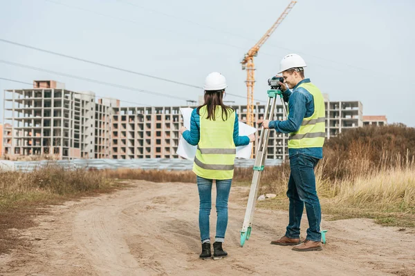 Surveyors working with blueprint and digital level on dirt road — Stock Photo