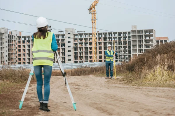 Arpenteurs mesurant le terrain sur un chemin de terre avec chantier en arrière-plan — Photo de stock
