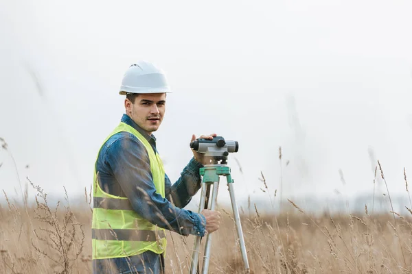 Vermessungsingenieur mit digitalem Pegel blickt auf Kamera im Feld — Stockfoto