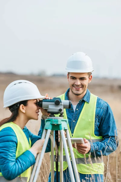 Sonrientes topógrafos que trabajan con nivel digital y tableta en el campo - foto de stock