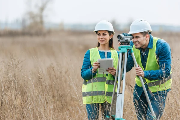 Sonrientes topógrafos con nivel digital y tableta en campo - foto de stock