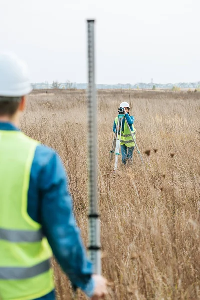 Selective focus of surveyors with digital level and ruler working in field — Stock Photo