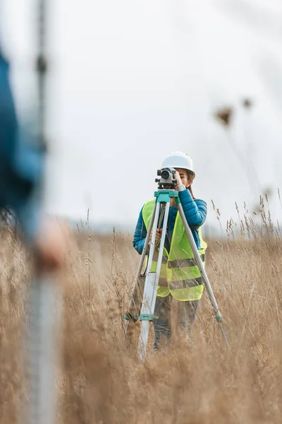 Selektiver Fokus der Vermessungsingenieure, die Land mit digitalem Pegel und Lineal im Feld messen — Stockfoto