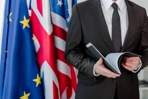 Cropped view of diplomat holding folder near flags — Stock Photo