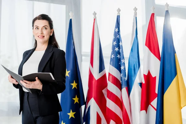 Cheerful ambassador holding folder near different flags — Stock Photo