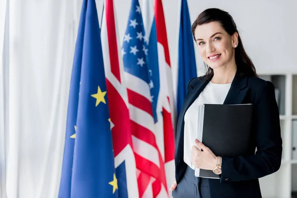 Smiling ambassador looking at camera near flags — Stock Photo