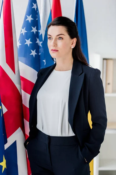 Beautiful diplomat standing with hands in pockets near flags — Stock Photo