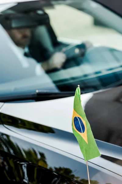 Enfoque selectivo de la bandera brasileña cerca del hombre en el coche moderno - foto de stock
