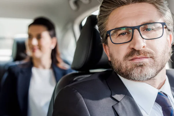 Selective focus of handsome ambassador looking at camera near diplomat in car — Stock Photo