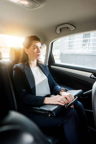 Selective focus of beautiful ambassador holding briefcase while sitting in car — Stock Photo