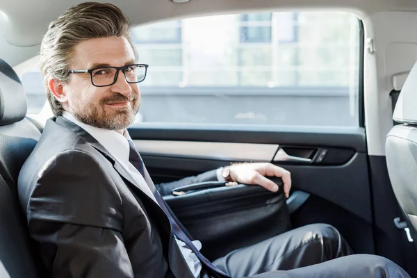 Happy diplomat in glasses sitting with briefcase in car — Stock Photo