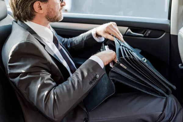 Обрезанный вид дипломата, держащего портфель и сидящего в машине — стоковое фото