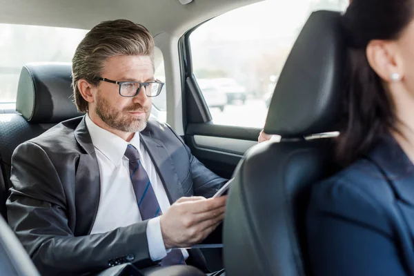 Foyer sélectif de beau diplomate dans des lunettes assis avec la femme dans la voiture — Photo de stock