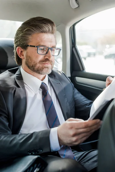 Selective focus of handsome diplomat holding folder in car — Stock Photo