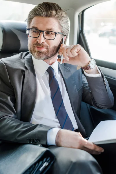 Selektiver Fokus eines gut aussehenden Diplomaten, der im Auto mit dem Smartphone spricht — Stockfoto