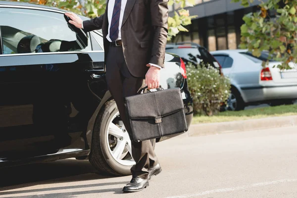 Ausgeschnittene Ansicht von Diplomat, der mit Aktentasche neben Auto steht — Stockfoto