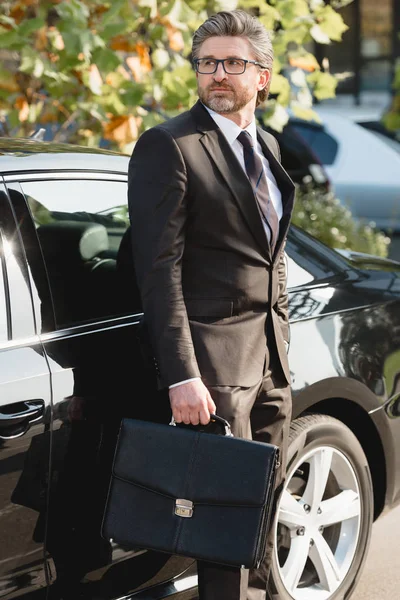 Бородатый дипломат в очках, с портфелем рядом с автомобилем — стоковое фото