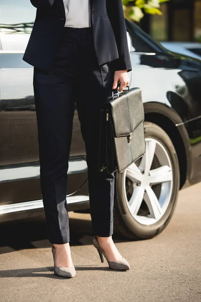 Cropped view of diplomat on heels standing near car with briefcase — Stock Photo