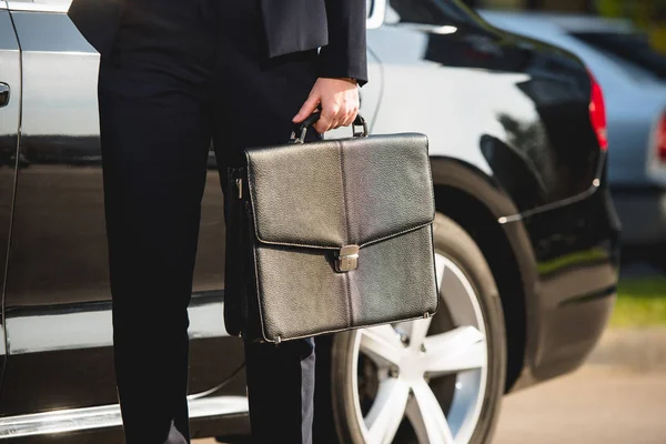 Обрезанный вид на посла, стоящего рядом с машиной с портфелем — стоковое фото