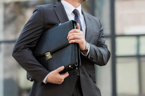 Vista recortada del hombre sosteniendo maletín de cuero fuera - foto de stock