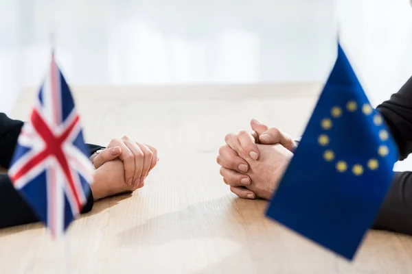 Vue recadrée des ambassadeurs assis les mains serrées près de l'union européenne et des drapeaux du royaume uni — Photo de stock