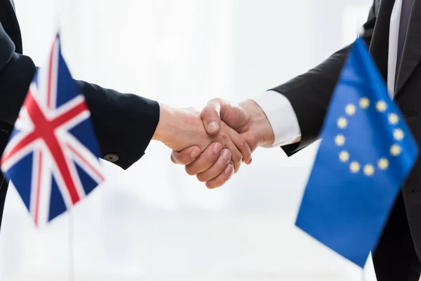 Vista cortada de diplomatas apertando as mãos perto da união europeia e bandeiras do reino unido — Fotografia de Stock