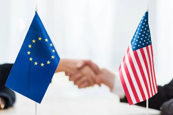 Foco seletivo de bandeiras dos EUA e união europeia perto de diplomatas apertando as mãos — Fotografia de Stock