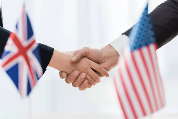 Enfoque selectivo de los diplomáticos estrechando las manos cerca de banderas de EE.UU. y el reino unido - foto de stock