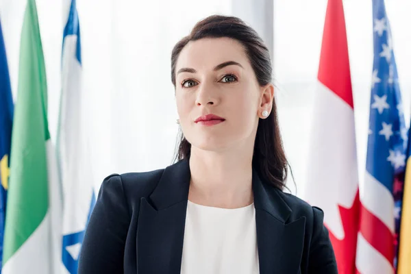 Attractive diplomat looking at camera near flags — Stock Photo