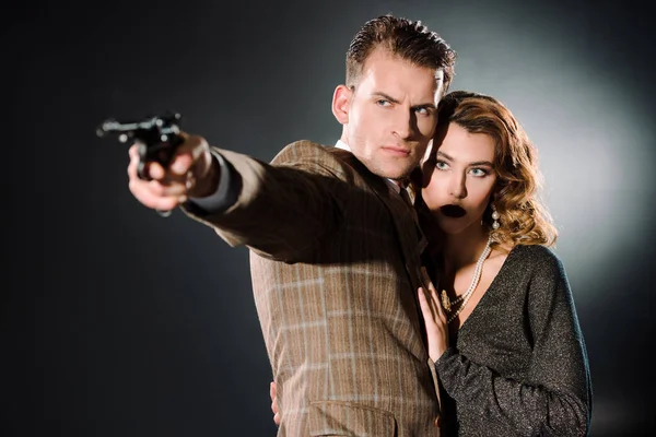 Attractive woman standing near armed gangster with gun on black — Stock Photo