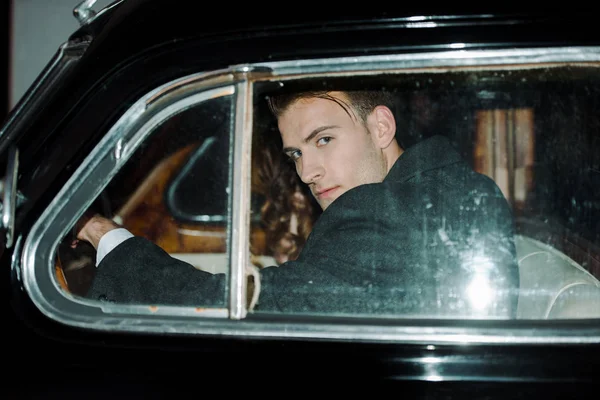 Hombre guapo y peligroso mirando a la cámara mientras está sentado en el coche — Stock Photo